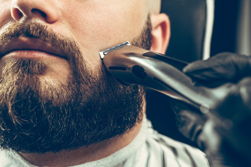 Barbershop client. Man getting his beard trimmed with electric razor